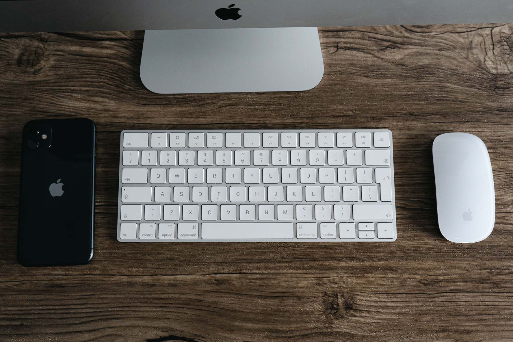Tastatur, Smartphone und Maus auf einer hölzernen Schreibtischplatze