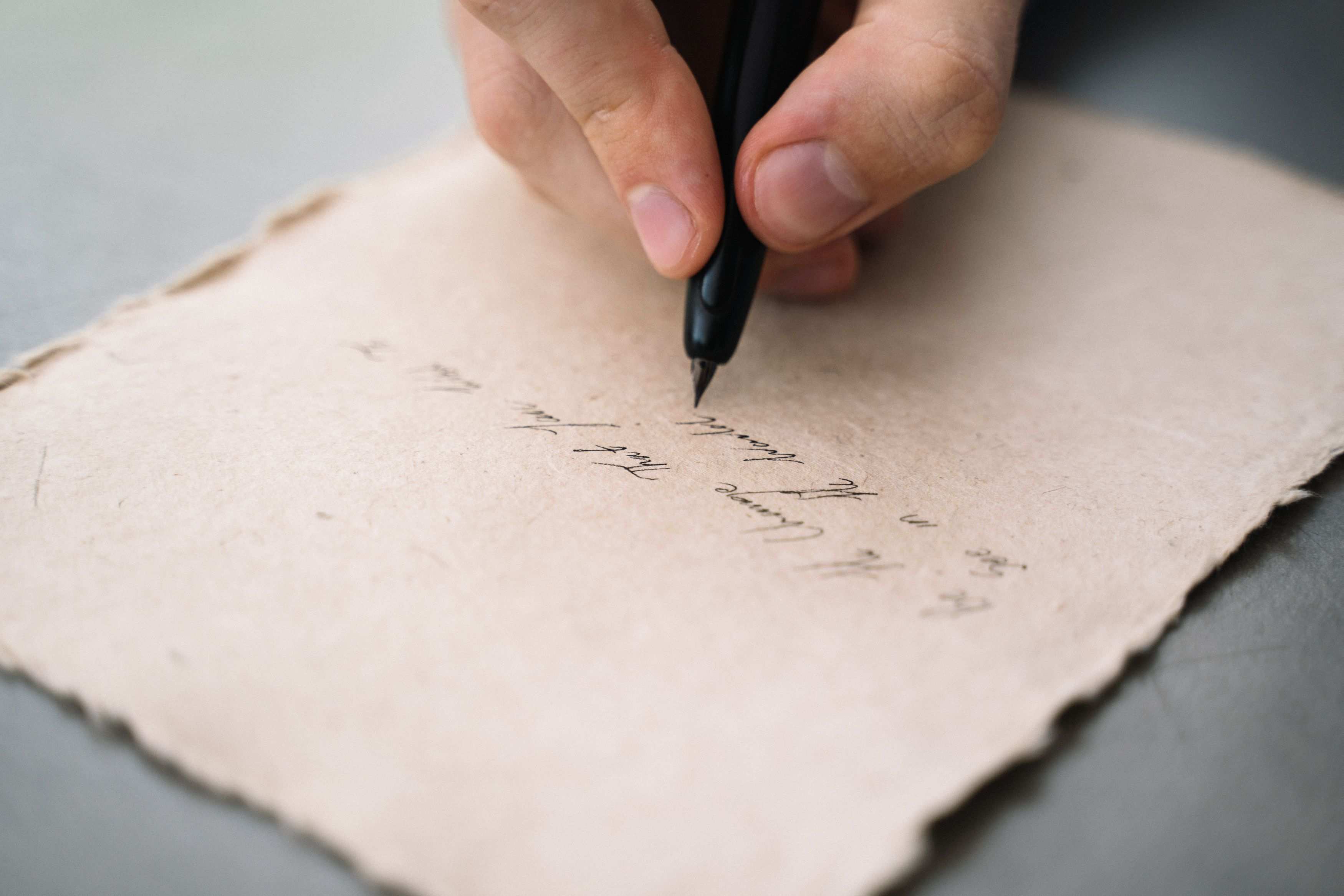 Nahaufnahme einer Hand, die mit einem schwarzen Stift auf strukturiertem Papier schreibt